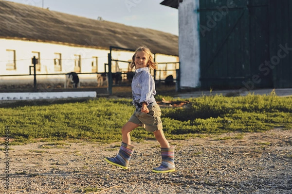 Obraz Horizontal photo of smiling farmer kid walking on a farm in summer. Happy childhood in the countryside. Copy space for text
