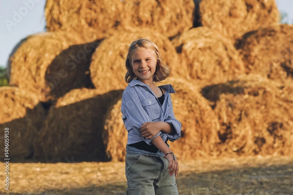 Obraz Horizontal portrait of smiling kid girl on the farm posing near rolls of hay bales, summertime in countryside, childhood and dreams