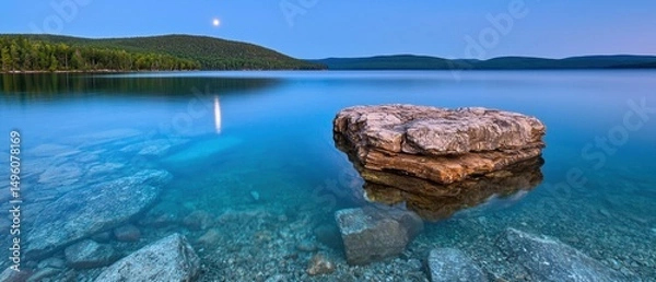 Obraz A serene lake at dusk, with a rocky outcropping and a distant mountain range.