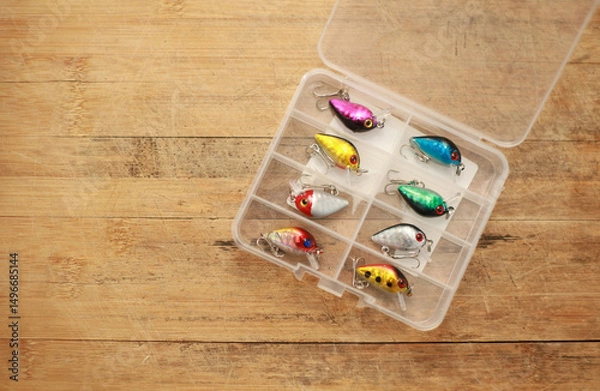 Fototapeta Fishing lures are in a plastic box on a wooden floor with space for copying.