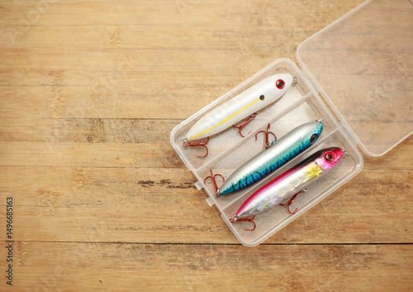 Fototapeta Fishing lures are in a plastic box on a wooden floor with space for copying.