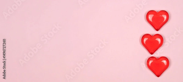 Fototapeta three red hearts made of semi-transparent plastic on a pastel-colored background with copy space on the left