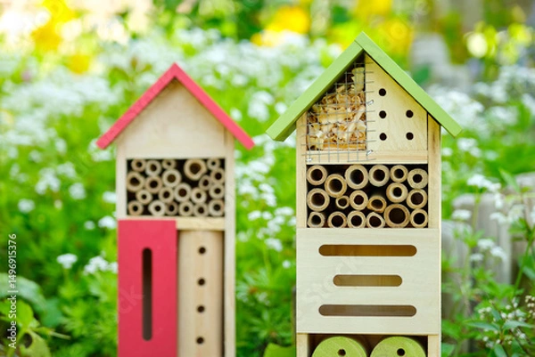 Fototapeta Two insect hotels or bee hotels in a summer garden with flowers. An insect hotel is a manmade structure created to provide shelter for insects in a variety of shapes and sizes and materials.	