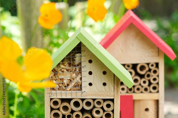 Fototapeta Two insect hotels or bee hotels in a summer garden with flowers. An insect hotel is a manmade structure created to provide shelter for insects in a variety of shapes and sizes and materials.	