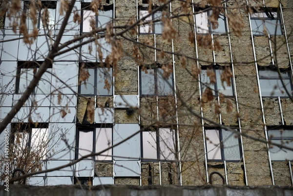 Fototapeta View of a damaged high rise building exterior in Kyiv with defocused leafy tree in the foreground
