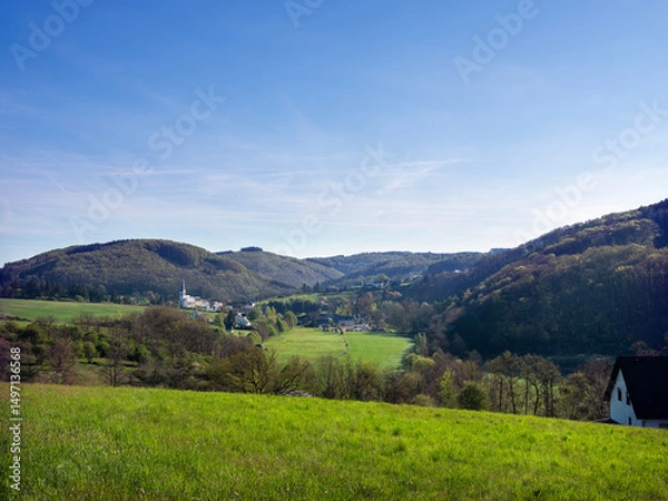 Fototapeta village with typical church in german suedeifel under blue sky in spring
