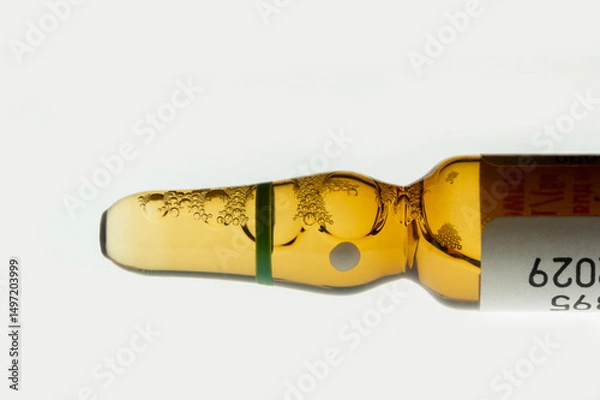 Fototapeta Golden medical ampoule with bubbles on white background. Close-up of glass ampoule with liquid and foam. Medical container with yellow liquid.
