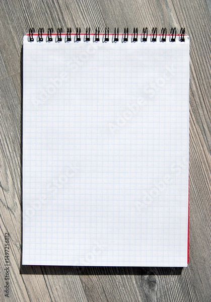 Fototapeta A blank notebook on a wooden background. A checked blank note page for a copy.