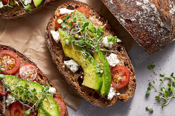 Obraz Sliced avocado and tomato on whole grain bread with sprouts  