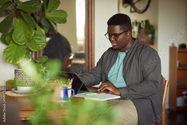 Fototapeta Young African man working remotely from home on a tablet