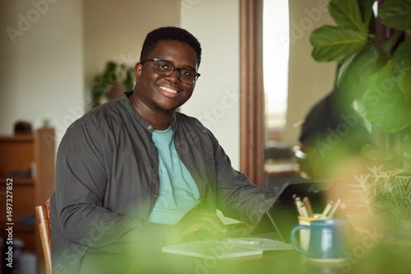 Fototapeta Young African man smiling while working from home on a tablet