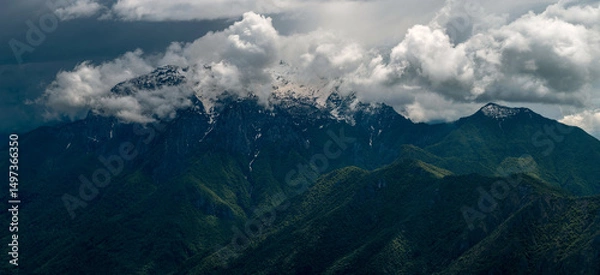 Fototapeta Expansive panorama showcasing Grigna Settentrionale and Pizzo della Pieve, with dramatic light illuminating the vibrant green slopes below, contrasted against high-contrast clouds above. Lombardy