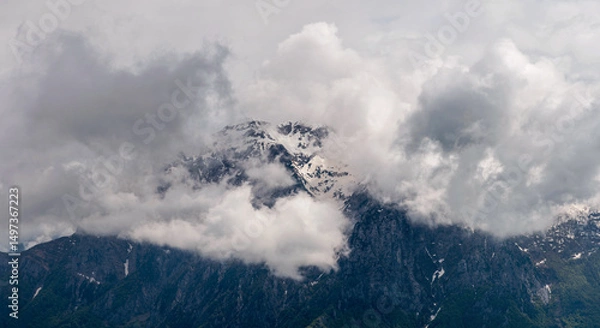 Fototapeta Majestic panorama of Grigna Settentrionale (Grignone) and Pizzo della Pieve, their imposing rocky summits partially veiled by swirling clouds, creating a mysterious alpine atmosphere. Lombardy