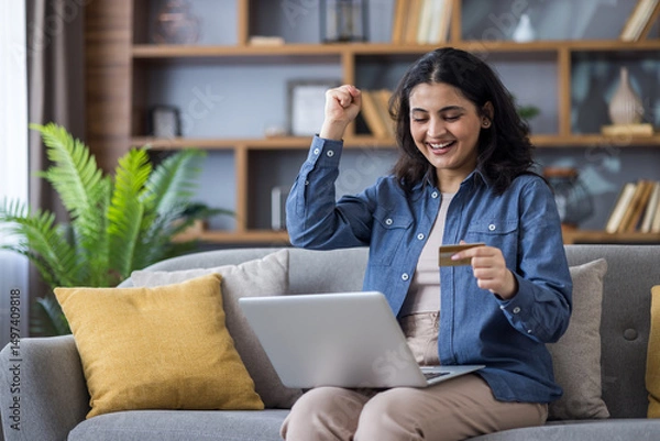 Obraz A woman smiles with excitement as she makes an online purchase using her laptop and credit card.
