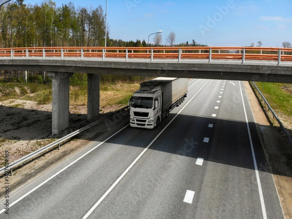 Fototapeta Truck drives under an overpass on a clear day along a quiet highway in a rural area