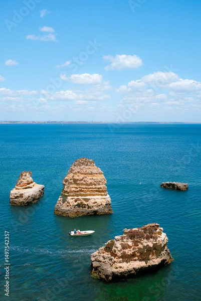 Fototapeta 16 June 2016 - Lagos, Portugal: aerial view of a man steering a dinghy between sea stacks. Person on a boat at sea. Bright summer day in the Algarve.