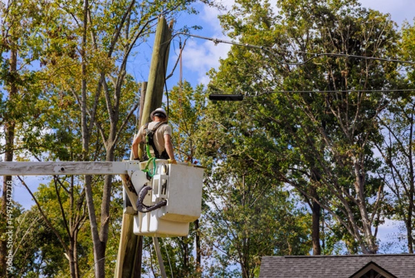 Obraz Utility worker stands in bucket lift fixing electrical lines above neighborhood with after hurricane
