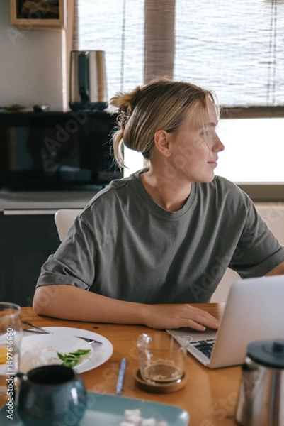 Obraz  Gen Z woman working from home at cozy kitchen table with laptop and phone. Digital nomad lifestyle, mindfulness, remote work, balance, mental calm and modern freelancing