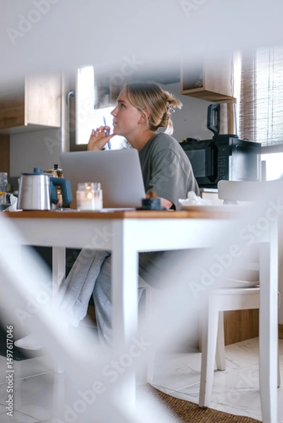 Obraz  Gen Z woman working from home at cozy kitchen table with laptop and phone. Digital nomad lifestyle, mindfulness, remote work, balance, mental calm and modern freelancing