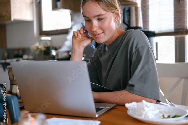Obraz  Gen Z woman working from home at cozy kitchen table with laptop and phone. Digital nomad lifestyle, mindfulness, remote work, balance, mental calm and modern freelancing