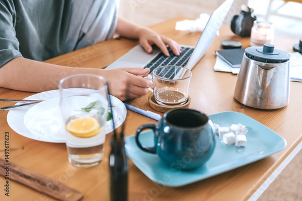 Obraz  Gen Z woman working from home at cozy kitchen table with laptop and phone. Digital nomad lifestyle, mindfulness, remote work, balance, mental calm and modern freelancing