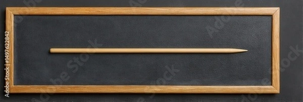 Fototapeta A single, light-colored pencil rests centrally on a dark slate board within a wood frame.