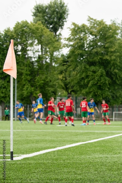 Fototapeta Two teams in red and blue uniforms battle for possession on a vibrant green soccer field. Players are strategically positioned, showcasing their athleticism and teamwork
