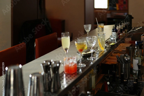 Fototapeta Bar counter with multiple cocktail glasses, some containing drinks, and bar tools, close-up