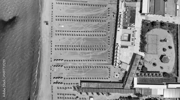 Fototapeta Drone shot of a vibrant beach club with rows of umbrellas and clear blue sea in the background