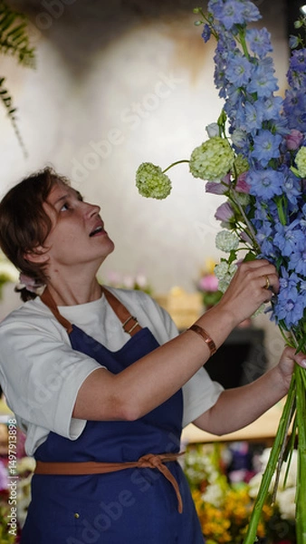 Fototapeta A florist in a flower shop makes a bouquet of blue delphiniums. Small business.  Close-Up.  Soft focus.