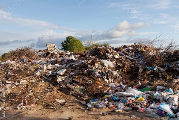 Fototapeta A large pile of mixed waste and garbage at a landfill site under a partly cloudy sky, illustrating environmental pollution.