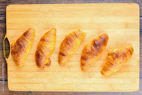 Obraz Top view of freshly baked croissants on wooden cutting board.