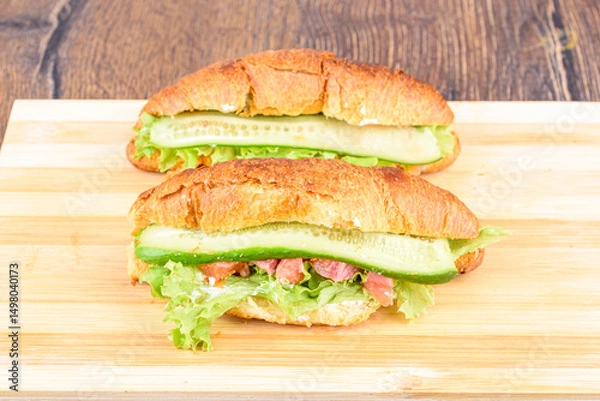 Obraz Croissants with lettuce, soft cheese and red fish with cucumber on a cutting board.