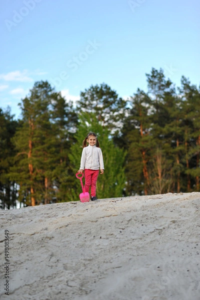 Obraz Child girl with two ponytails playing with shovel in the sand outdoor on nature in the spring. Outdoor activities. Copy space for text