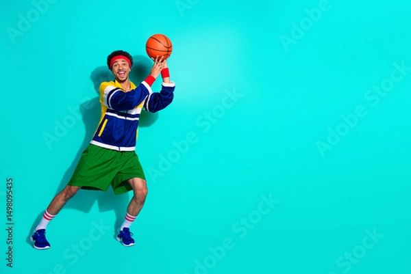 Fototapeta Energetic young man in vibrant retro sportswear gearing up for a basketball game against teal backdrop