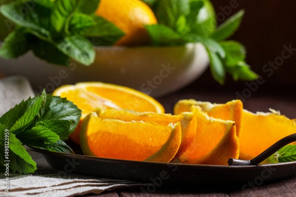 Fototapeta Oranges, lemons, limes, mint and lemon balm and raindrops illuminated by the sun on a wooden background.