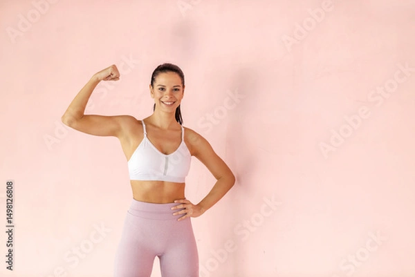 Fototapeta Young fit toned sportswoman in shape flexing muscles and smiling at the camera.