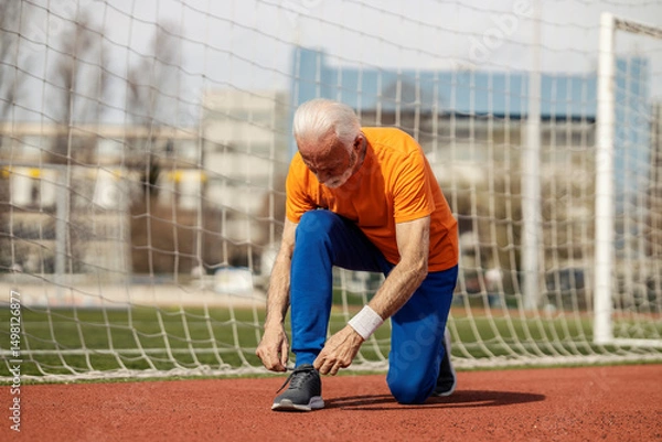 Fototapeta An old athlete is tying shoelace after workouts on stadium.