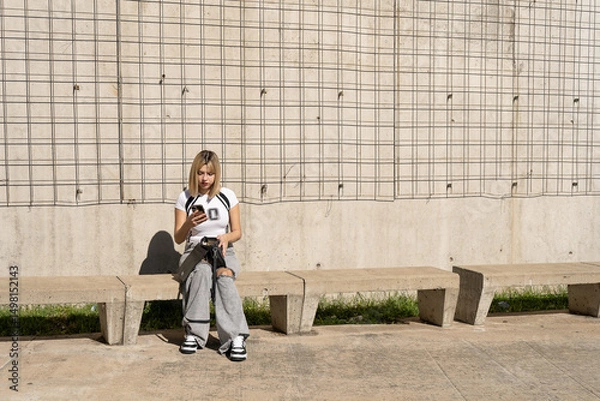 Fototapeta Young woman opening her bag while sitting on concrete bench