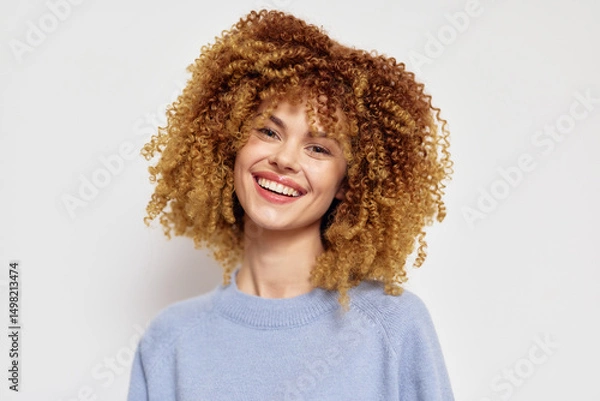 Fototapeta Smiling young woman with curly hair wearing a light sweater against a neutral background Her joyful expression adds warmth to the image, highlighting her personality and charm