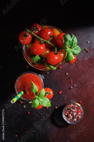 Fototapeta Creative flat lay with tomato juice and basil next to a bowl of multicolored heirloom tomatoes and colorful peppercorns on dark background