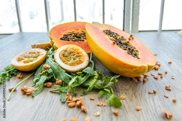 Obraz Slices of sweet papaya, maracuja, green rucola surrounded by granola flakes on a wooden background