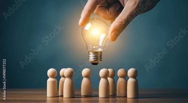 Obraz A hand holds a glowing lightbulb over a group of wooden figurines