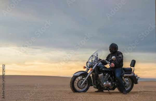 Fototapeta Man on motorcycle in desert during sunset with dramatic clouds — concept of freedom, travel, solitude, adventure, and outdoor lifestyle in wild open landscapes