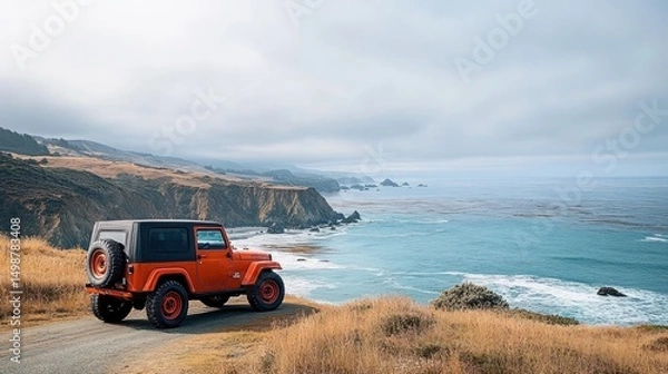 Obraz orange off-road vehicle parked on a coastal dirt road overlooking the ocean with rocky cliffs and grassy hills under a cloudy sky