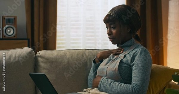 Fototapeta A tired woman working remotely from home has a video conversation with her supervisor. Lying on the couch, she shows her medication to clarify her health situation and recovery progress.