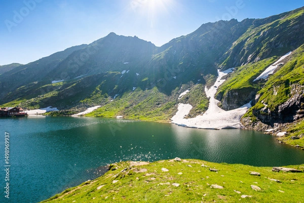 Fototapeta balea lake of romania. alpine landscape of fagaras mountains with pond. sunny weather with clouds on the blue sky above carpathians. snow and grass on the hillside in summer. vacation season