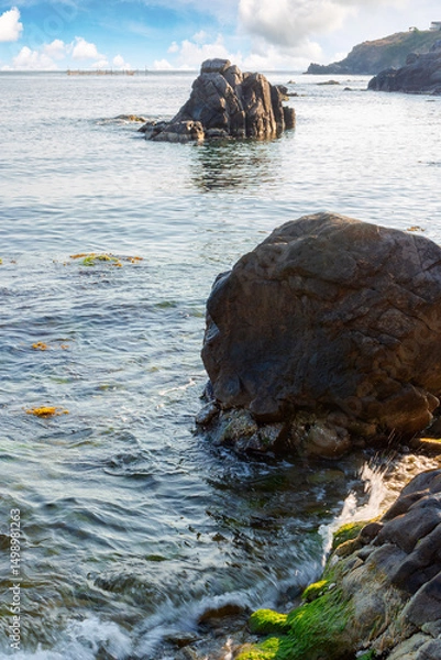 Fototapeta seascape with rock in the water. textured boulder reflecting calm sea surface in morning light. vacation season in summer. sunny weather. fluffy clouds above horizon
