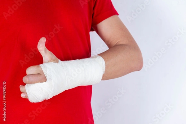 Fototapeta Medical Concepts. Closeup of Body Parts of Caucasian Man in Red Shirt with Broken Hand In Plaster and Bandaid Isolated on White