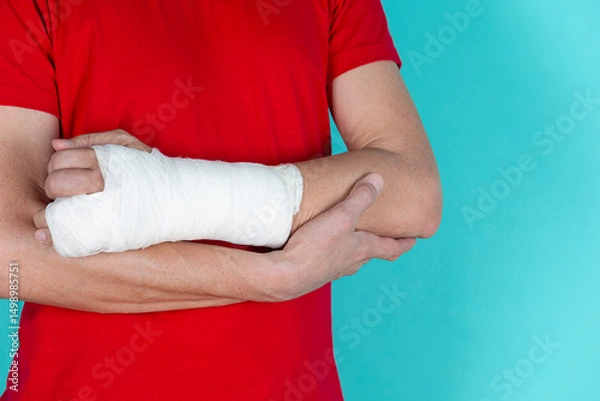 Fototapeta Medical Concepts. Closeup of Caucasian Man Damaged Broken Hand In Plaster and Bandaid Isolated on Turquoise Background.